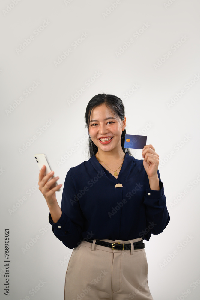 Confident Asian woman holding credit card and mobile phone standing on white background