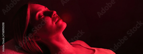 A woman reclines, enjoying red light therapy for wellness or cosmetic treatment. Female appears tranquil under the therapeutic glow, likely seeking rejuvenation or healing.