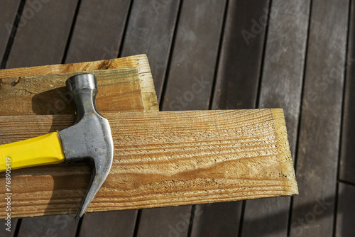 A metal hammer with a yellow and black wooden handle on wooden planks in a room with dark wooden floors