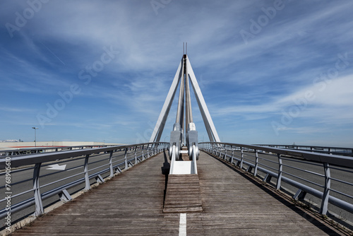 Bridge with wooden pedestrian walkway floor with paint marks and metal braces to support the structure on a day with blue skies