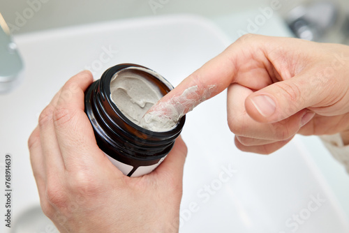 female hand takes a clay face mask from a jar. home spa