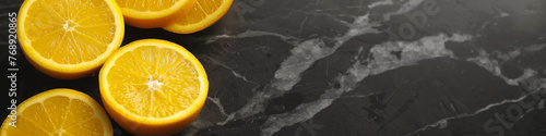 A close up of a black marble counter top with a few oranges on it. The oranges are cut in half and arranged in a row