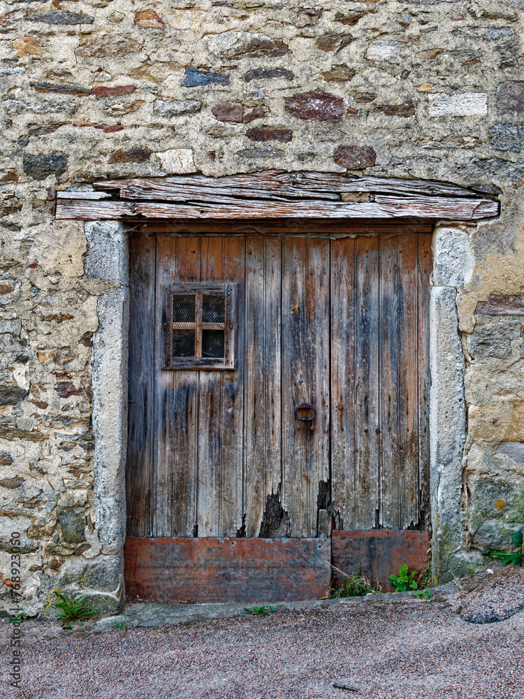 Aged wooden door with a small window opening, on an ancient stone wall