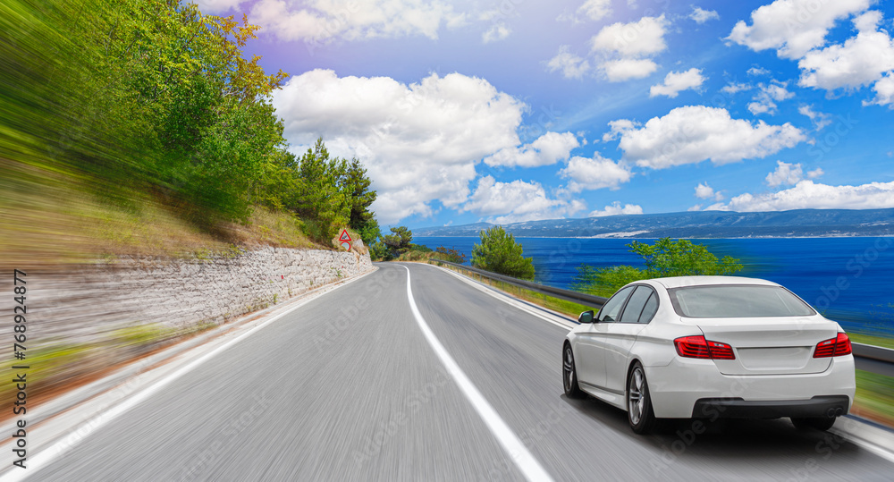 A white car drives along the sea coastline on a sunny summer day.