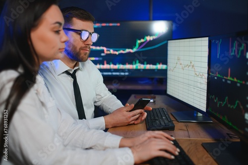 Team of stockbrokers are having a conversation in a dark office with display screens