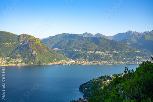 A beautiful mountain range with a lake in the foreground. The lake is calm and the mountains are covered in trees. The sky is clear and the sun is shining brightly. The scene is peaceful and serene © pyty