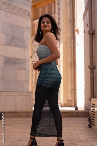 A woman in a blue and white dress stands in front of a building