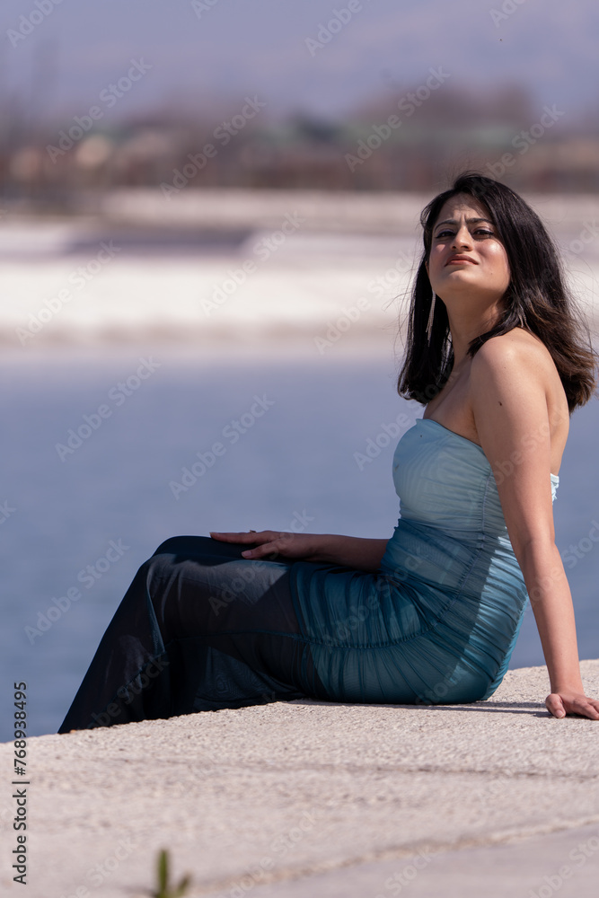 A woman in a blue dress is sitting on a ledge by a body of water