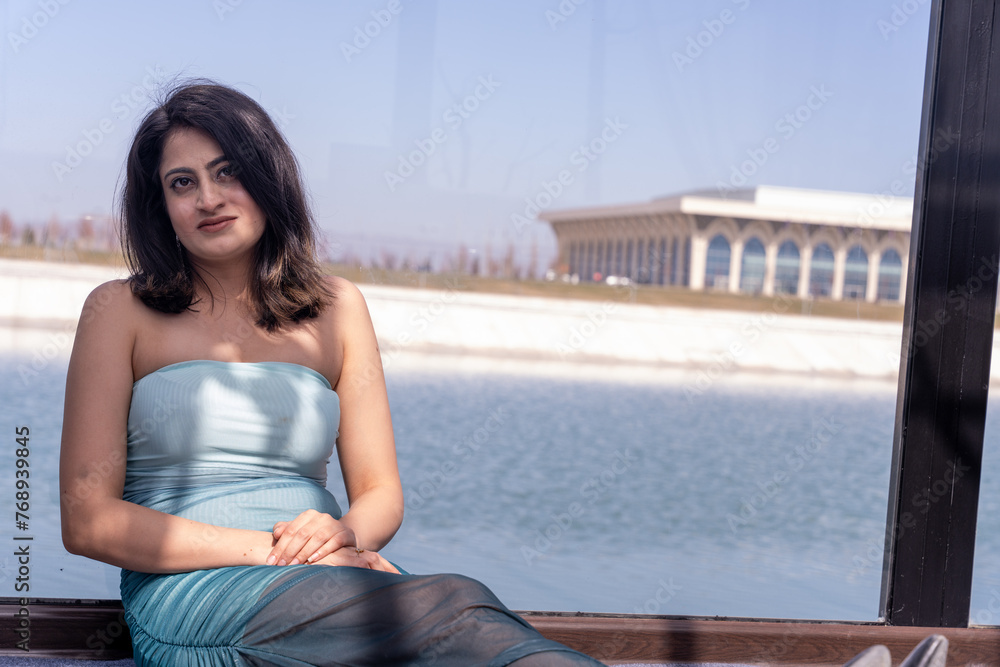 A woman in a blue dress is sitting on a boat by a lake