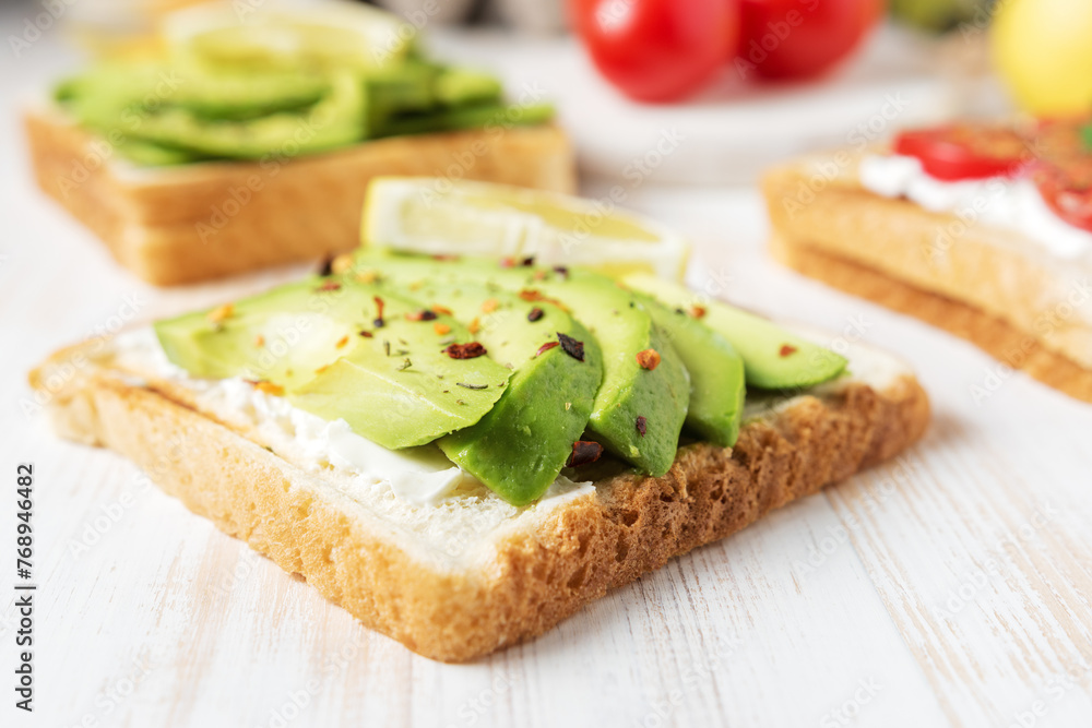 Sliced avocado on toast bread with spices on white wooden background. Food concept.