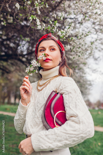Portrait of woman wearing red hair scarf in spring park. Retro female fashionable accessories. Headscarf and purse