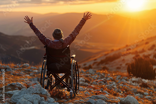 An individual in a wheelchair with arms uplifted, basking in a sunset surrounded by mountains