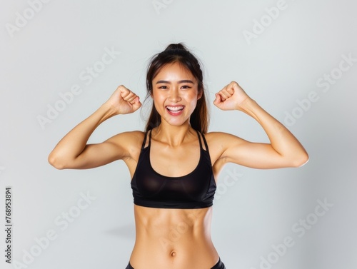 Happy Asian Thai woman smiling wear black sportswear with bun hair, raising arms, showing muscles power. © Restyler