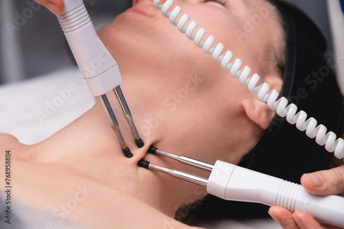 Close-up of a woman receiving an electric neck massage with equipment in a beauty salon. Used for therapy with a multifunctional electro massage device