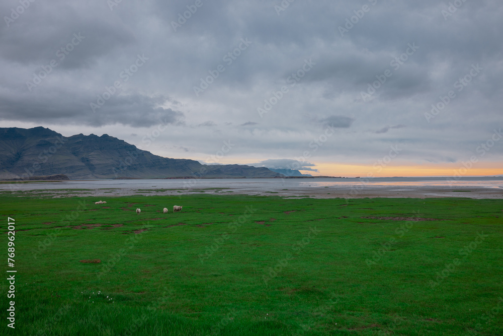 Obraz premium Beautiful icelandic landscape in early morning. Green grass, yellow sunrise, clouds and road in the distance. Very beautiful scenery around hvalnesviti