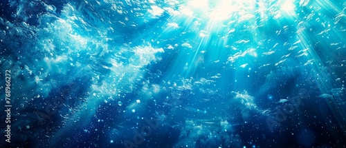   An underwater view of a blue ocean with sunlight filtering through the water and schools of fish swimming both below and on the surface