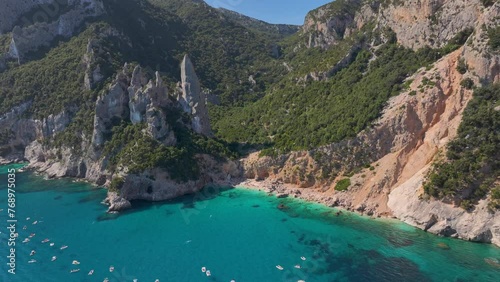 Aerial - Cala Goloritze mountain range on the coastline of Sardinia with cliffs rising up above the sea and small boats down in the water