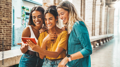 Three happy friends watching a smart phone mobile outdoors - Millennials women using cellphone on city street - Technology, social, friendship and youth concept