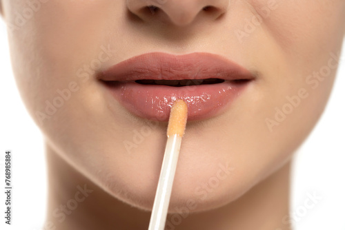 young beautiful woman apply a lip gloss on her lips on white background