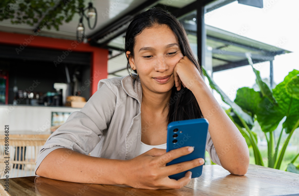 joven adolescente sentada en un café leyendo mensajes en su celular  - obrazy, fototapety, plakaty 