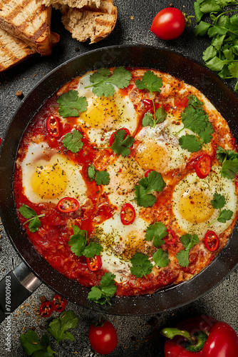 Tasty Shakshuka eggs in a pan with toast on a dark concrete background. Eggs poached  in a spicy tomato pepper sauce. Traditional Jewish scrambled eggs. Flat lay, Top view.