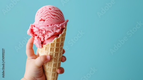 Child's hand holding a melting pink ice cream in a waffle cone on a bright blue background. Summer refreshment and dessert concept for design and print
