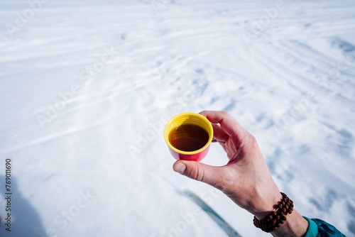 Small cup of coffee in nature, hand holding glass of tea on snow background, warming drink in winter.