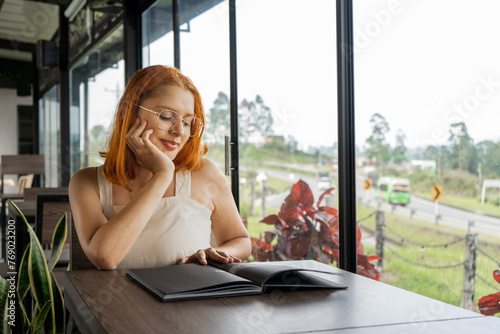 mujer joven latina con la mano junto a su rostro mientras revisa el menu de un restaurante a la orilla de la via principal  photo