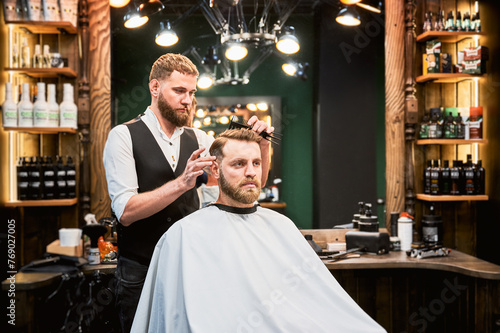 Hairdresser making final touches in new haircut. Comfortable atmosphere in modern barbershop. Stylish barber using professional comb to style hair.