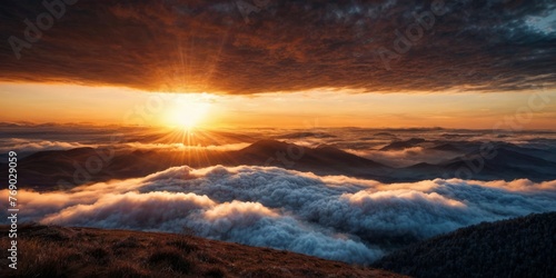  The sun descends behind mountains, casting clouds in the foreground and a backdrop of ranges