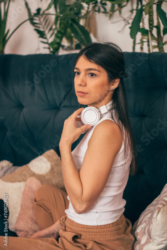 Thoughtful young dark-haired woman in casual clothes wearing headphones,sitting on the couch.Relaxation,meditation,listening music.