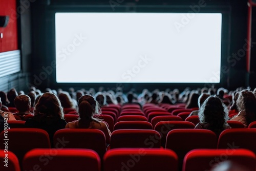 Cinema blank wide screen and people in red chairs in the cinema hall. Blurred People silhouettes watching movie performance © romanets_v