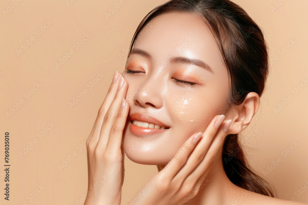 Beautiful smiling Asian girl model with natural makeup enjoys glowing hydrated skin on beige background closeup Beautiful smiling Asian girl model with natural makeup enjoys glowing hydrated skin on beige background closeup
