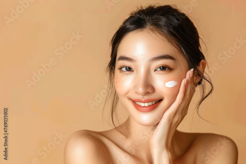 Beautiful smiling Asian girl model with natural makeup enjoys glowing hydrated skin on beige background closeup