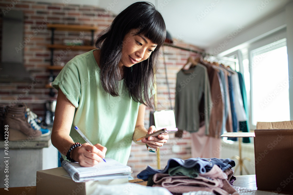 Smiling Asian woman packing clothes into a box at home Smiling Asian woman packing clothes into a box at home