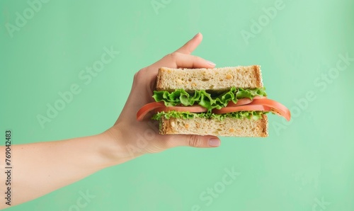 Toast sandwich with tomato and lettuce - The image portrays a lifestyle of health and time-saving, with a hand presenting a toast sandwich with fresh tomato and lettuce on a green backdrop photo