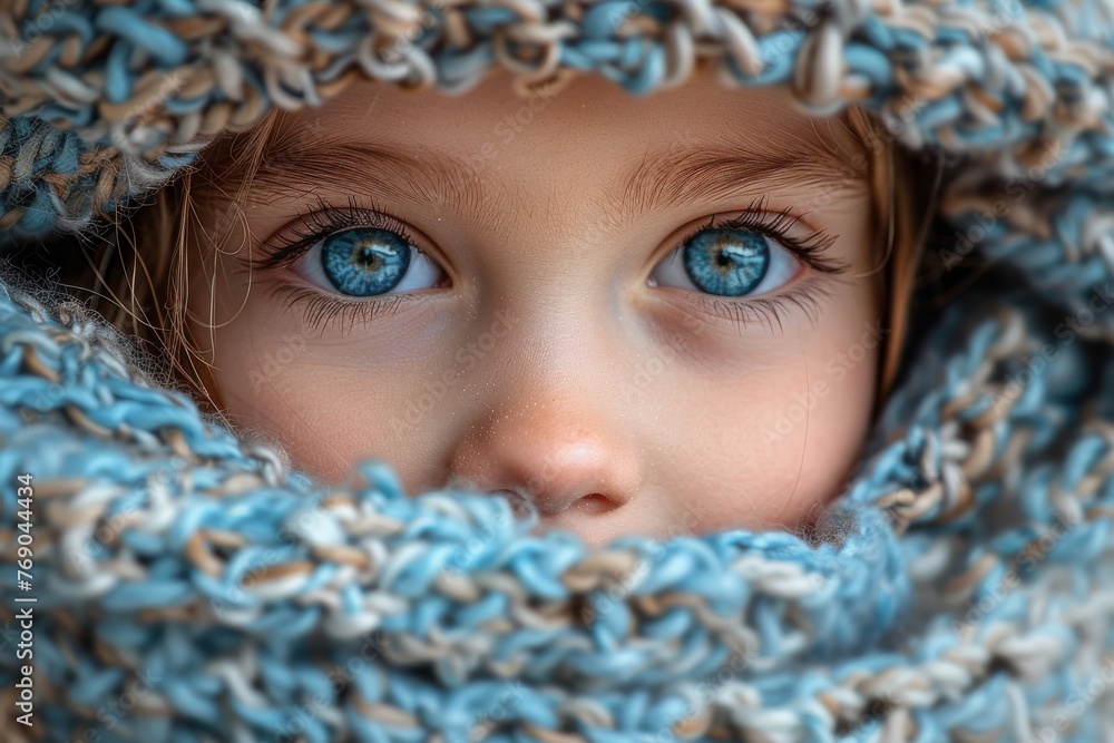 Young girl's bright blue eyes visible through the gap in a knit blue scarf Young girl's bright blue eyes visible through the gap in a knit blue scarf