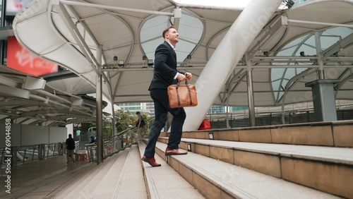 Smart caucasian businessman walking up stairs surrounded by urban view. Side view of ambitious project manager finding challenging job or investment opportunity at city with modern building. Urbane.