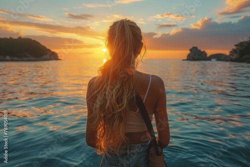 A lone woman with long hair gazes toward a gorgeous sunset with islands in the distance and calm sea waters