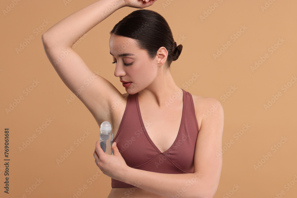 Obraz premium Beautiful woman applying deodorant on beige background