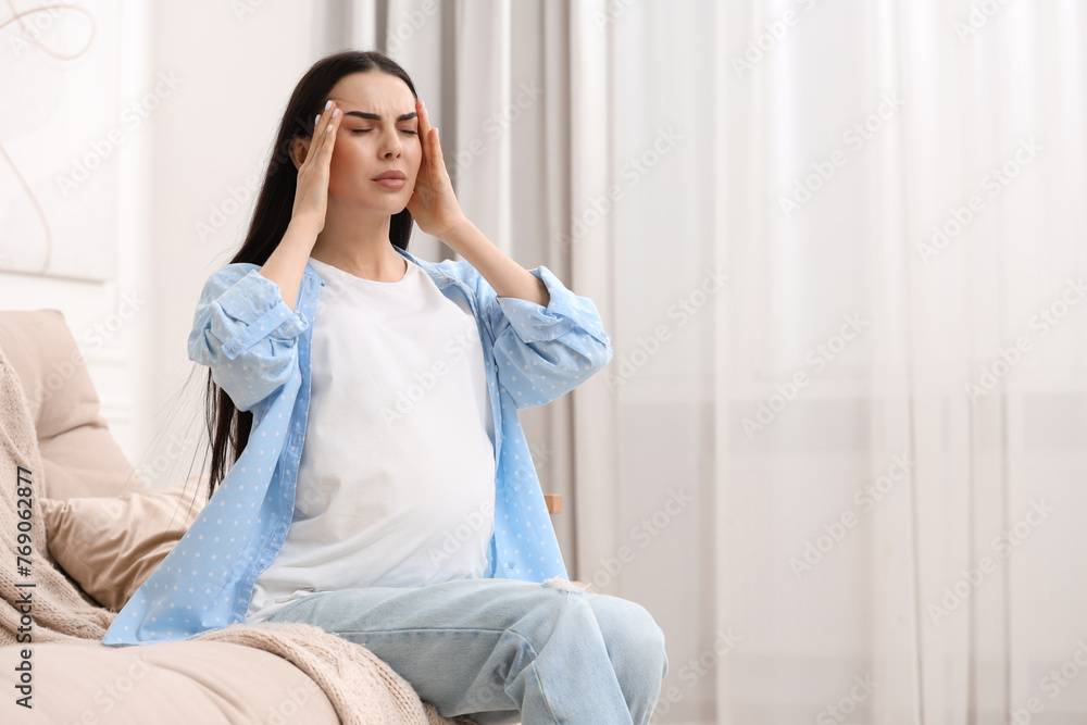 Pregnant woman suffering from headache on sofa at home, space for text Pregnant woman suffering from headache on sofa at home, space for text