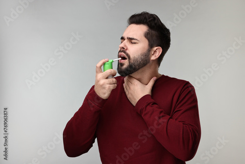 Young man using throat spray on grey background © New Africa