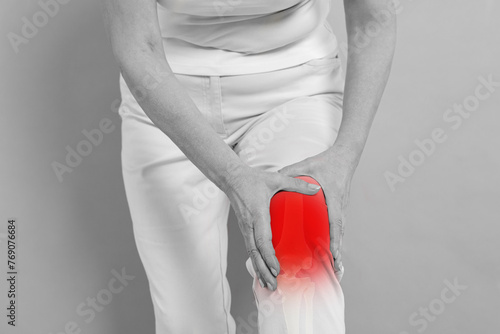 Arthritis symptoms. Woman suffering from pain in her knee on background, closeup. Black and white effect with red accent in painful area