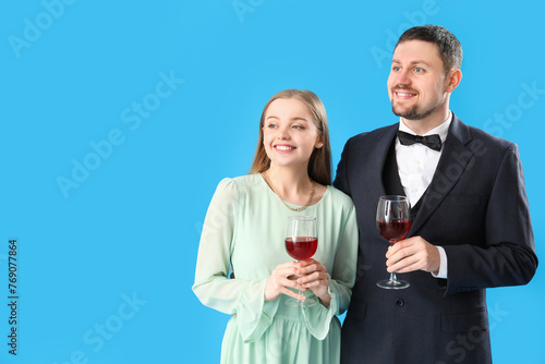 Elegant young couple with glasses of wine on blue background