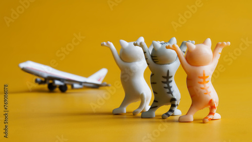 Three toy kittens with raised paws and passenger airplane on yellow background. Concept of seeing off an airplane flight and air passengers. Happy flight. Toy world. Photo photo