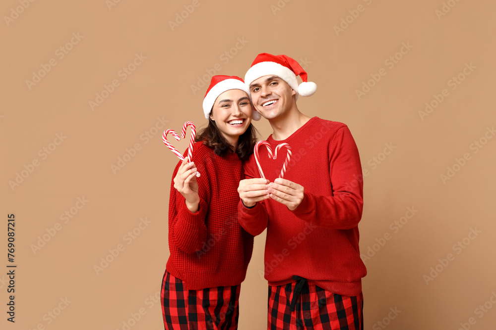 Happy young couple in Christmas pajamas and with candy canes on beige background Happy young couple in Christmas pajamas and with candy canes on beige background