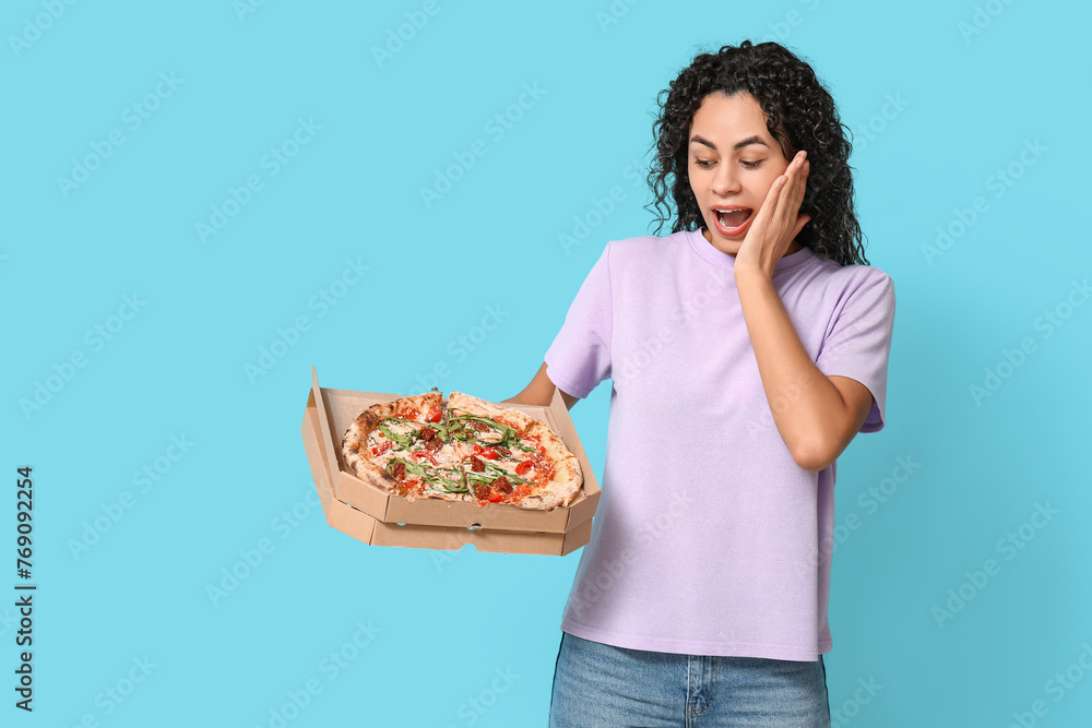 Beautiful young shocked African-American woman with delicious pizza on blue background Beautiful young shocked African-American woman with delicious pizza on blue background