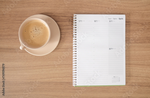 Xícara de café com agenda sob fundo de madeira. Cores claras, bege, amadeirado, caderno para deixar recado, escrever photo