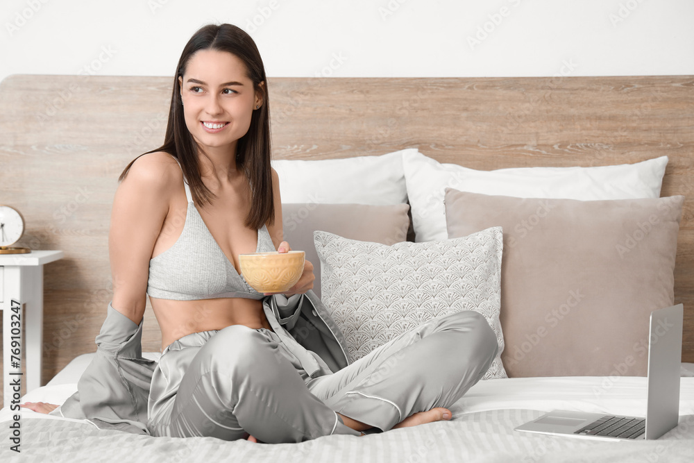 Sexy young woman with laptop drinking tea in bedroom - obrazy, fototapety, plakaty 