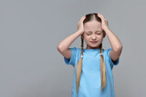 Little girl suffering from headache on grey background. Space for text